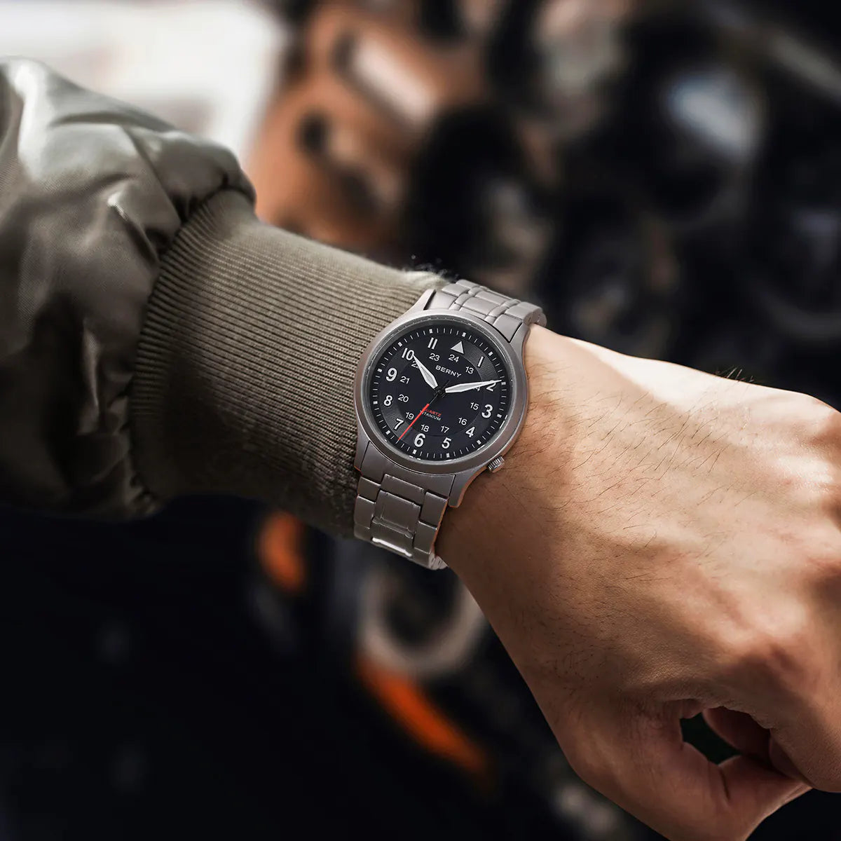 A Berny watch is shown on a person's wrist, featuring a sleek titanium bracelet and a black dial with both 12-hour and 24-hour markers. The watch is styled with a casual jacket, highlighting its versatile and modern design suitable for everyday wear.
